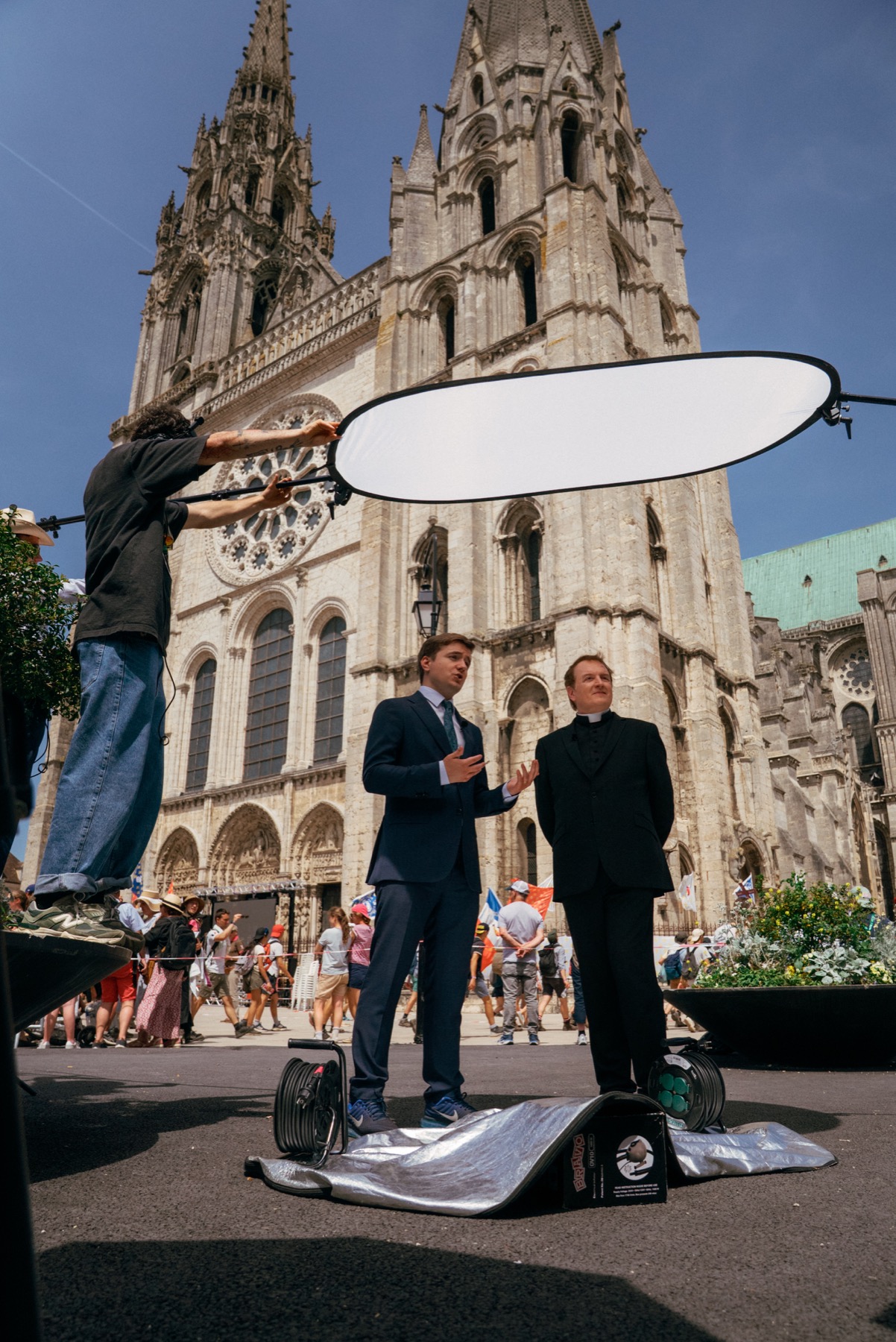 Field production at Chartres Cathedral with interview setup, reflector, crew, and clergy subject.