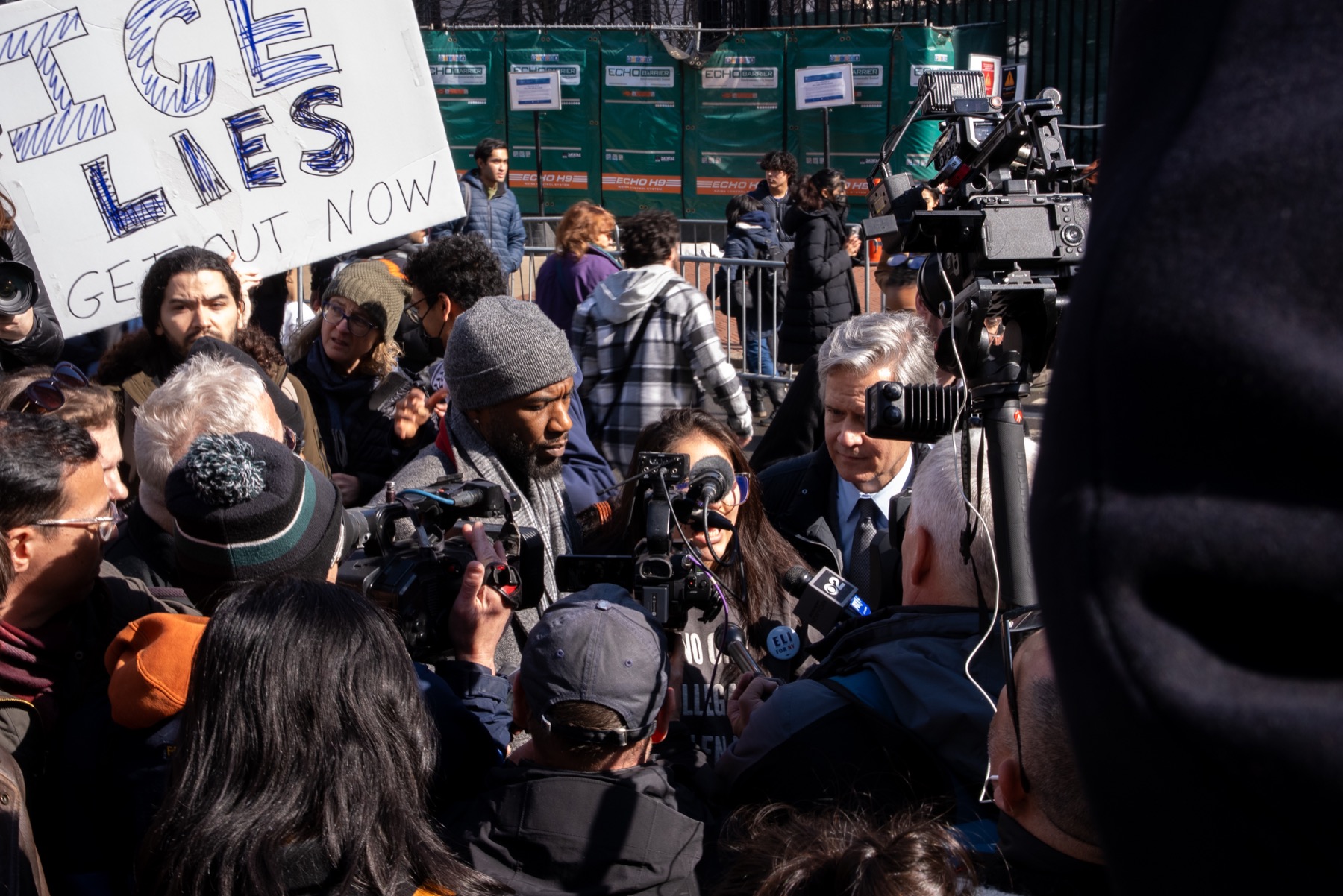Public-facing documentary coverage with press, cameras, microphones, and crowd presence.